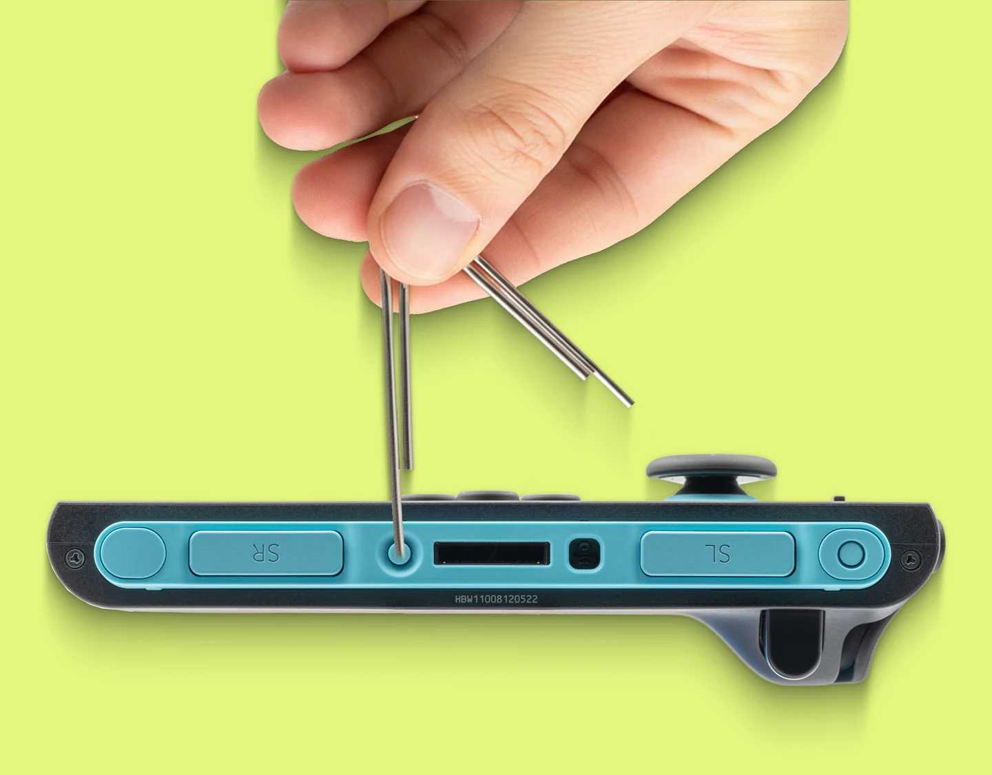 Hand pressing the small reset button on the back of a Nintendo Joy-Con with a paper clip.